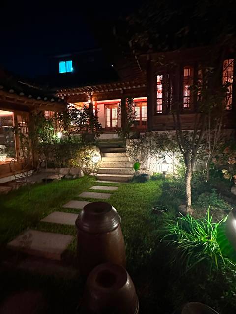 Night-time garden path with stone steps, plants and soft lantern lighting beside a hanok