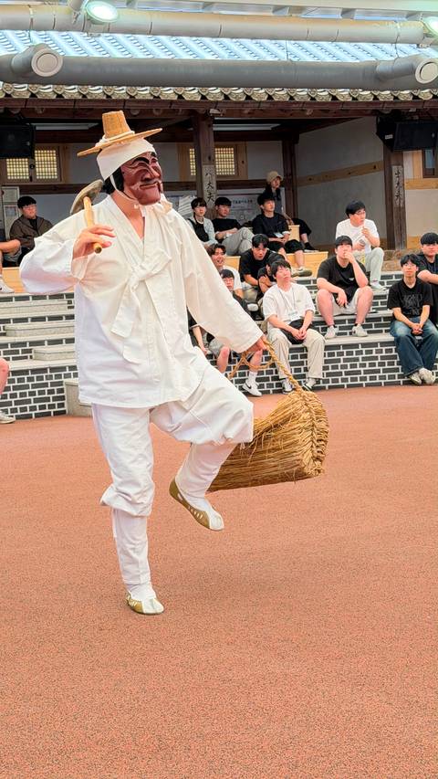 Performer dressed in white traditional costume dancing with a straw basket before onlookers