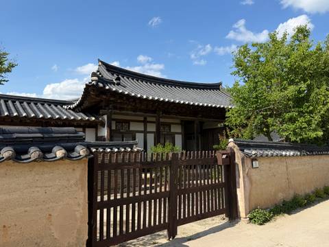 Repeating view of a Korean hanok with tiled roof and wooden gate on a sunny day