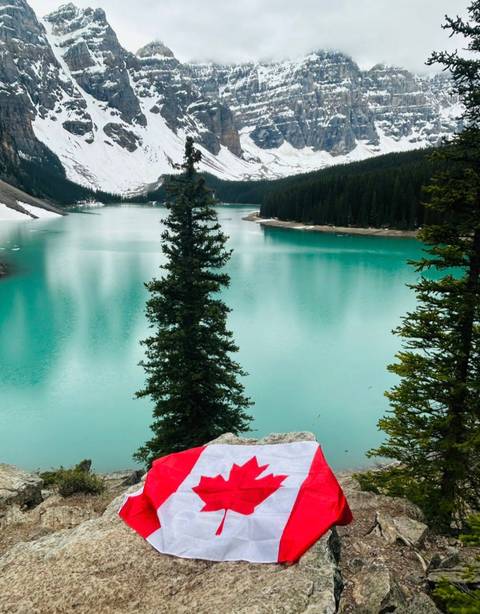 A vivid turquoise glacial lake seen beyond evergreen trees and steep mountain sides.