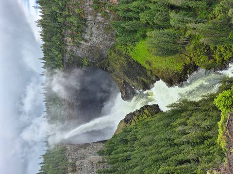 Helmcken Falls plunging into a deep misty canyon surrounded by lush green forest under cloudy skies.