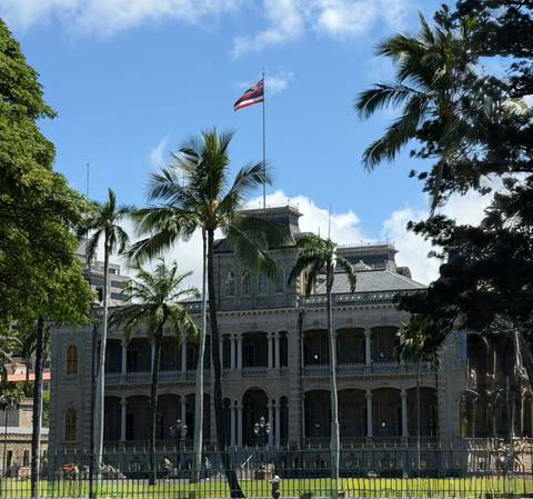 Iolani Palace framed by palm trees under a blue sky