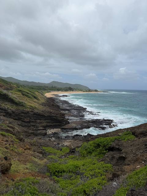 Rugged rocky coastline with waves crashing and distant sandy beach