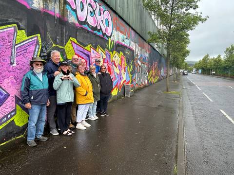 Tour group posing in front of colourful graffiti on the Belfast Peace Wall on a wet street