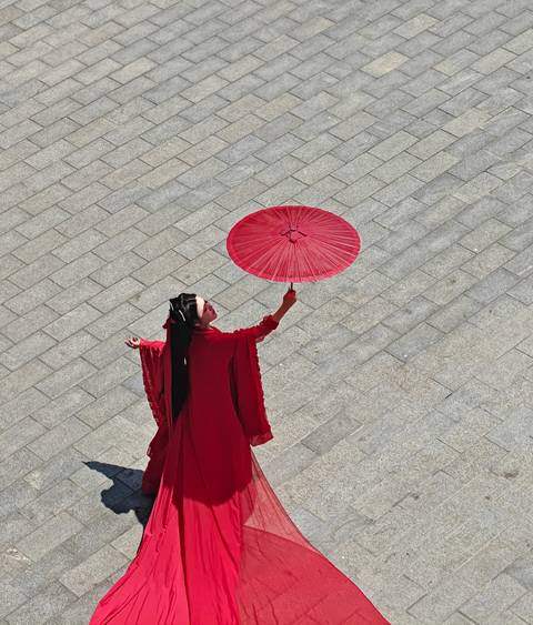 Woman in flowing red traditional dress holding a red umbrella viewed from above