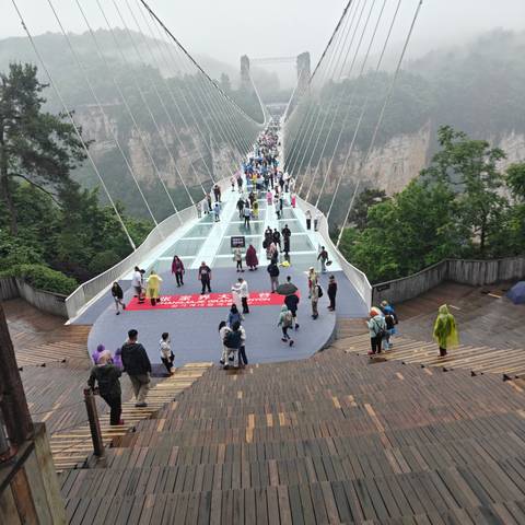 Crowds walking across the glass Zhangjiajie Grand Canyon bridge suspended above the valley