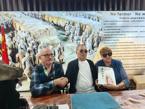 Three men sitting at a table shaking hands with terracotta warrior backdrop
