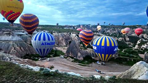 Dozens of colorful hot air balloons drift over the surreal rock formations of Cappadocia at dawn