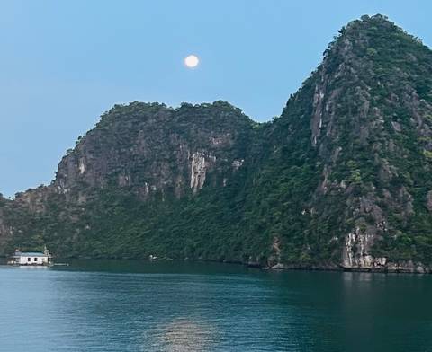 Moon rising above dramatic limestone karst cliffs over calm emerald water