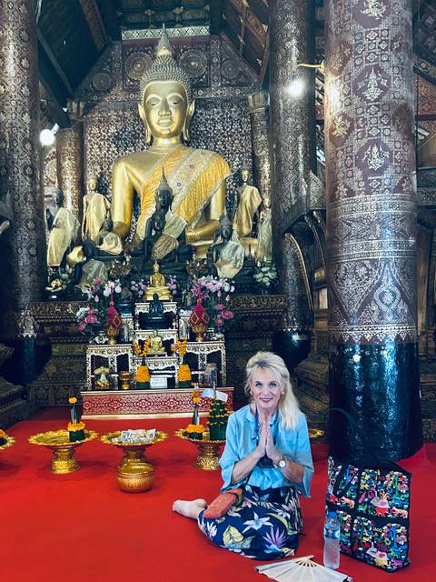 Visitor inside ornate Buddhist temple with golden statues and intricate carvings in Luang Prabang