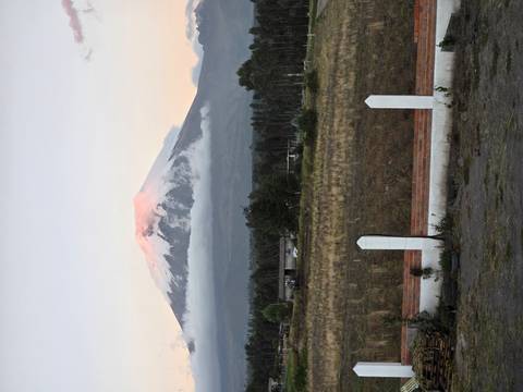 Snow-capped Cotopaxi volcano rises above clouds at sunrise over rural highlands.