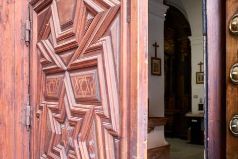 Close-up of an ornately carved wooden church door partially open to an interior with crosses.