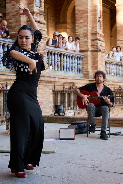 Flamenco dancer in black polka-dot attire performs while a guitarist plays in the background.