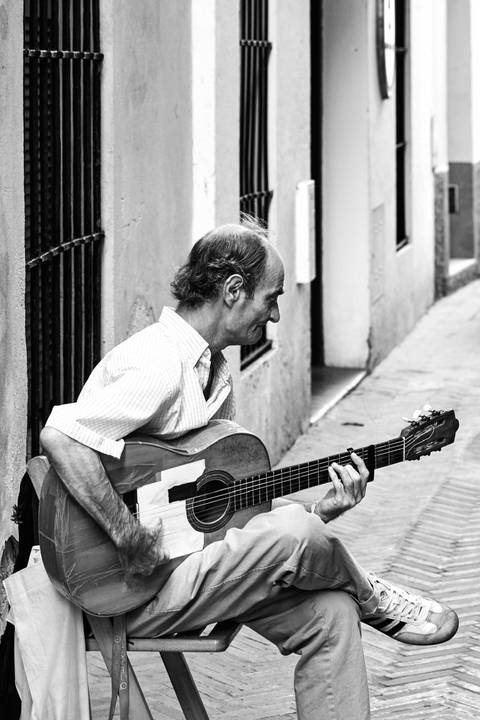 Black-and-white portrait of a street guitarist playing an acoustic guitar.