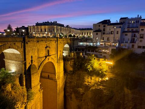 Night view of Puente Nuevo bridge in Ronda dramatically lit above the gorge with town lights.