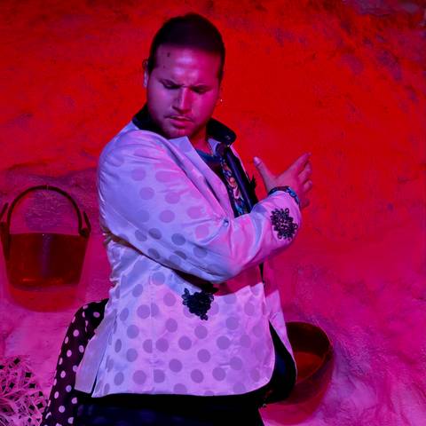 Portrait of a male flamenco dancer in polka-dot jacket against vivid red backdrop.