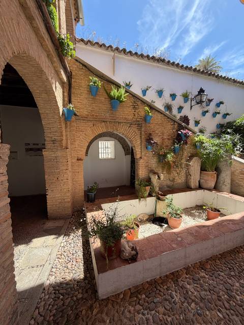 Quiet courtyard with brick arch and blue flowerpots hanging on white walls.