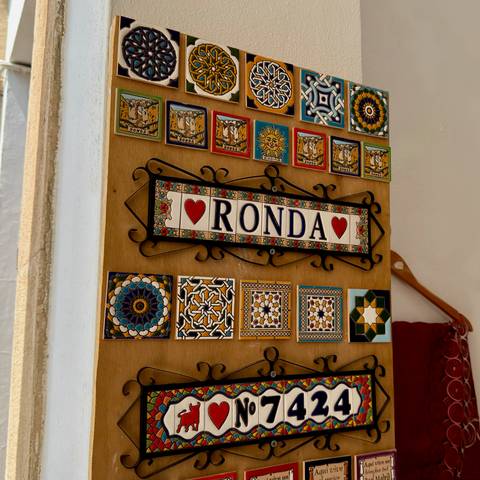 Wooden display of colourful ceramic tiles with a souvenir sign reading 'Ronda'.