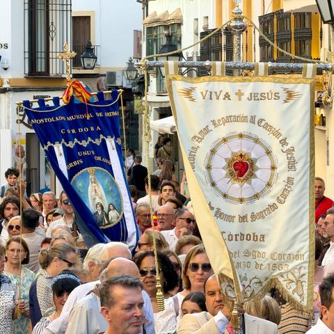 Crowded religious procession with ornate fabric banners bearing sacred images and text.