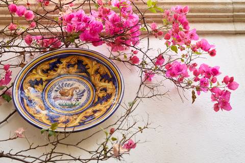 Decorative ceramic plate mounted on a wall with bright pink bougainvillea branches.
