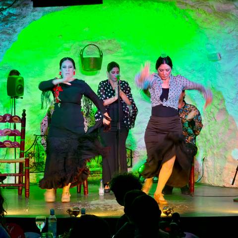 Three female flamenco dancers in vibrant lighting captured mid-movement on stage.