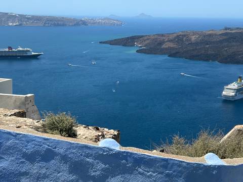 Deep blue caldera waters with cruise ships and speedboats viewed from whitewashed Santorini cliff.