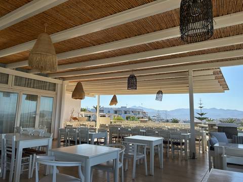 Open-air terrace with white wooden tables and woven lampshades overlooking distant mountains under a clear sky.