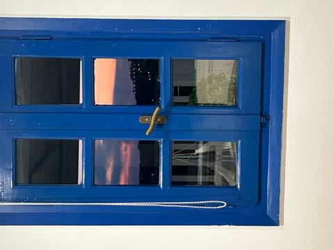 Blue-framed window reflecting a pink evening sky and distant lights.