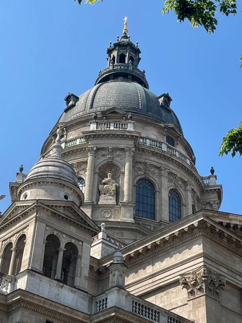 Upward view of St. Stephen's Basilica dome with marble statues against a clear blue sky.