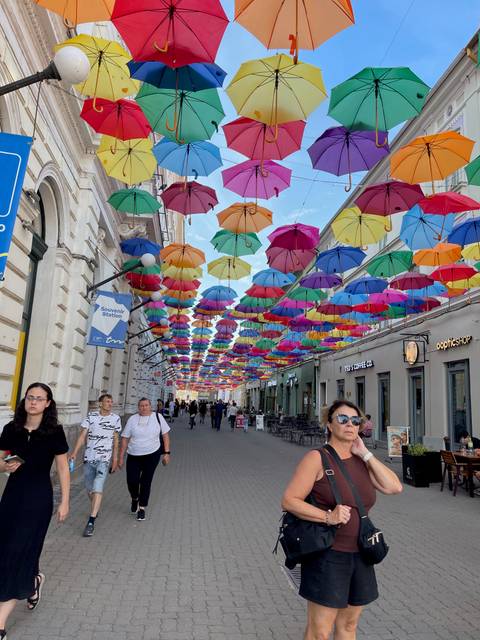 Pedestrian street festooned with colorful umbrellas hanging overhead, lined with cafes and shops.