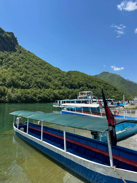 Tour boats dock beside emerald lake surrounded by steep green mountains under a clear blue sky