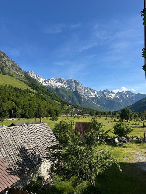 Panoramic view of alpine valley village with snow-streaked peaks towering above lush meadows