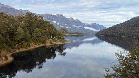 Serene fjord-like lake flanked by forested mountains with mist floating in valleys.