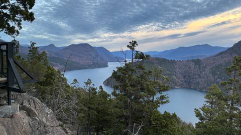 Panoramic viewpoint over a winding lake surrounded by hills under evening sky hues.