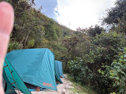 Green camping tents set up along a jungle trail with a finger partially obscuring the lens.