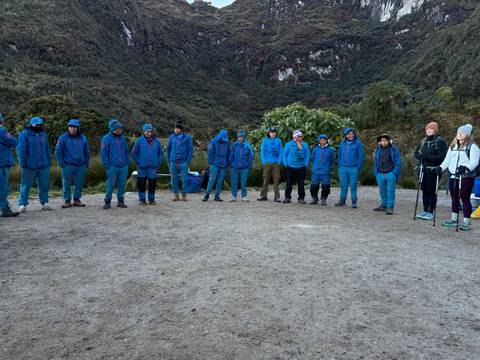 Line of porters and guides in blue uniforms standing together on a clearing along the Inca Trail.