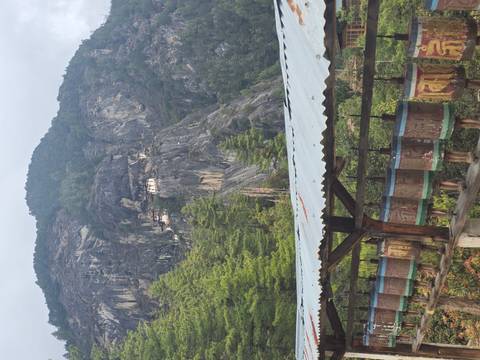 Prayer wheels line a covered walkway with Tiger’s Nest monastery clinging high on a cliff in the distance.