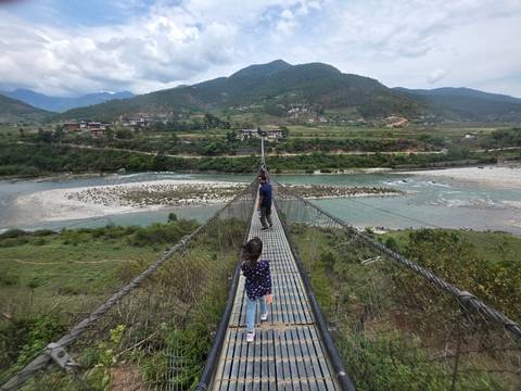 People walk across a long swaying suspension bridge high above a turquoise river and valley.