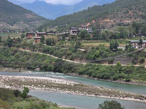 Wide valley scene with traditional Bhutanese houses scattered along terraced fields beside a winding river.