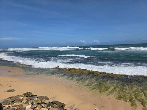 Waves crash onto a sandy tropical beach with clear aqua shallows under a bright blue sky.