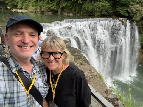 A smiling couple poses for a selfie in front of the cascading Shifen Waterfall in Taiwan.