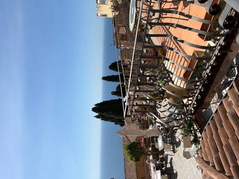A Mediterranean terrace with wrought-iron railings overlooks the deep blue sea and distant cypress trees.