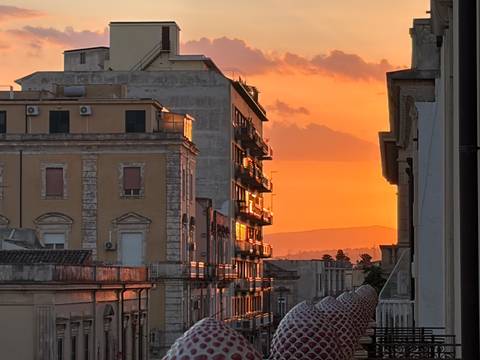 Orange sunset light reflects off city buildings and clouds between narrow streets in Sicily.