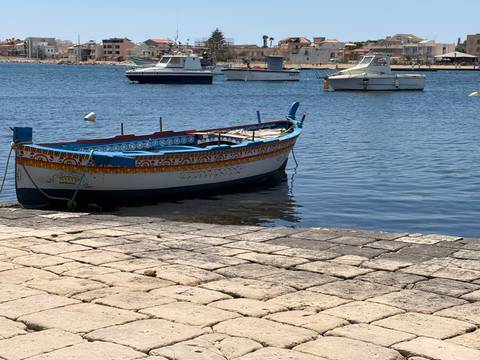 Traditional painted fishing boat floating on calm blue harbour water with other small boats and a coastal town behind