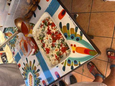 Tray of lasagna being assembled with tomato sauce and ricotta on a colourful tiled table