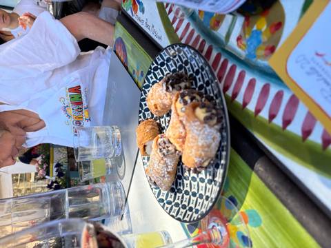 Plate of mini cannoli dusted with sugar on a patterned dish, with a participant wearing an apron in soft focus