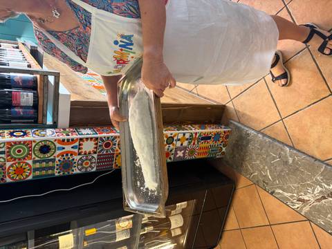 Person in apron holding a metal tray covered with flour-dusted fish inside a quaint kitchen space