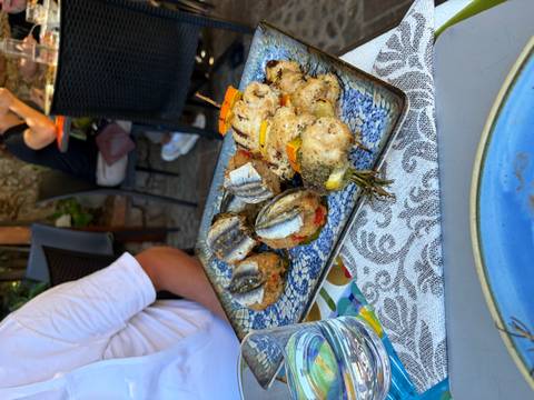 Grilled fish rolls and rosemary-topped skewers on a blue platter at an outdoor restaurant table