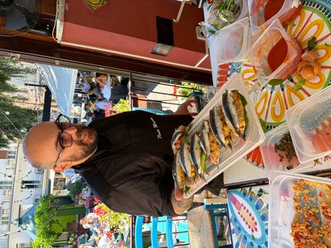 Chef proudly holding a tray of stuffed sardines at a cooking station with colourful tablecloths