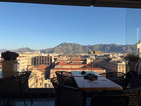 Panoramic rooftop view over Palermo’s historic buildings with mountain backdrop at clear dusk